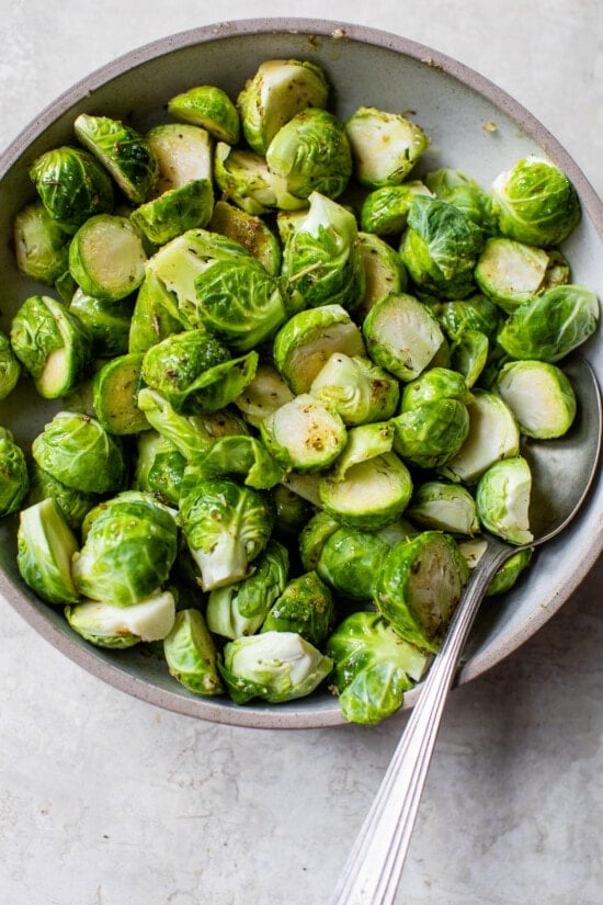 Brussels sprouts in a bowl with olive oil and seasonings.